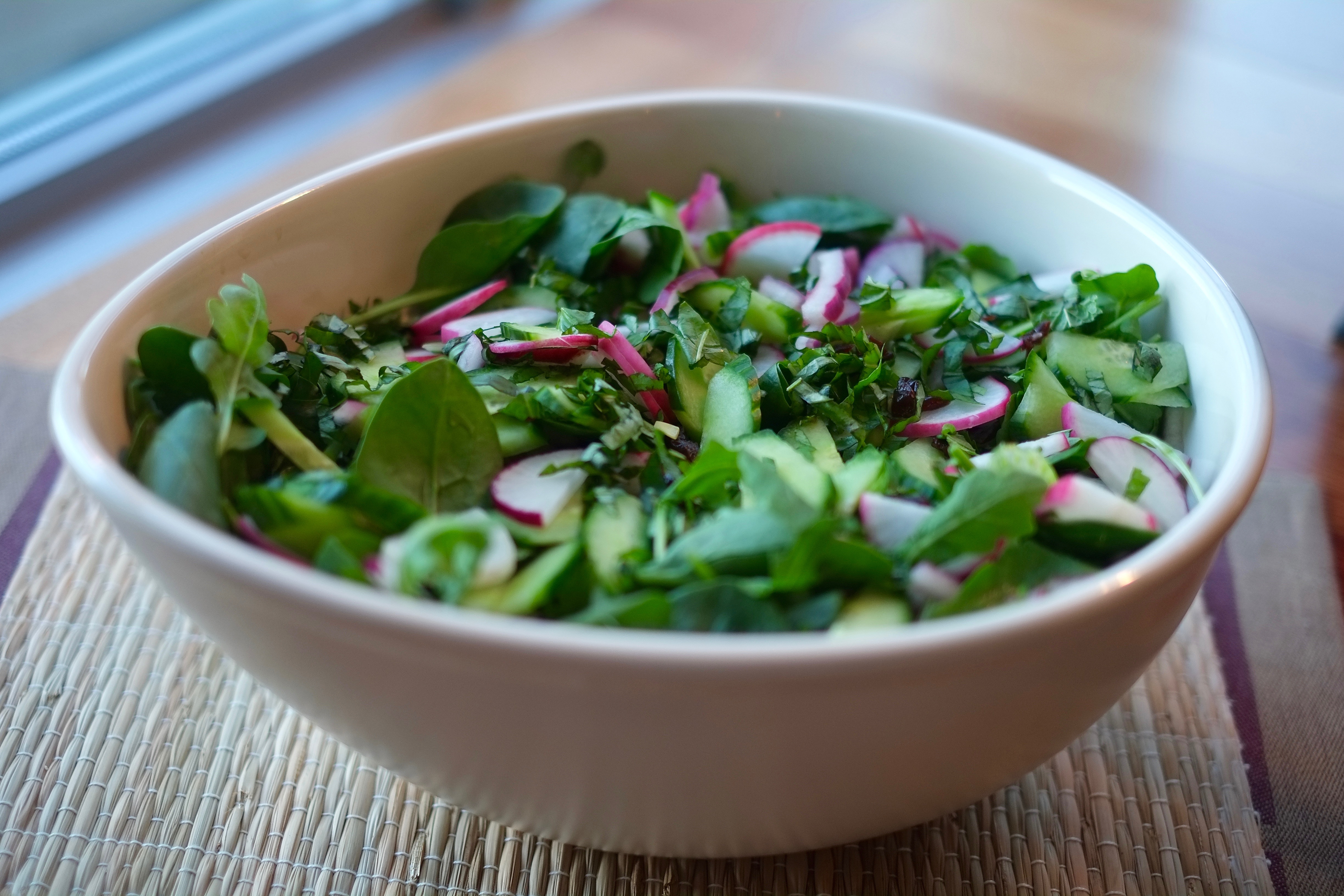 Big green tossed salad in an oval bowl with radishes and red onion