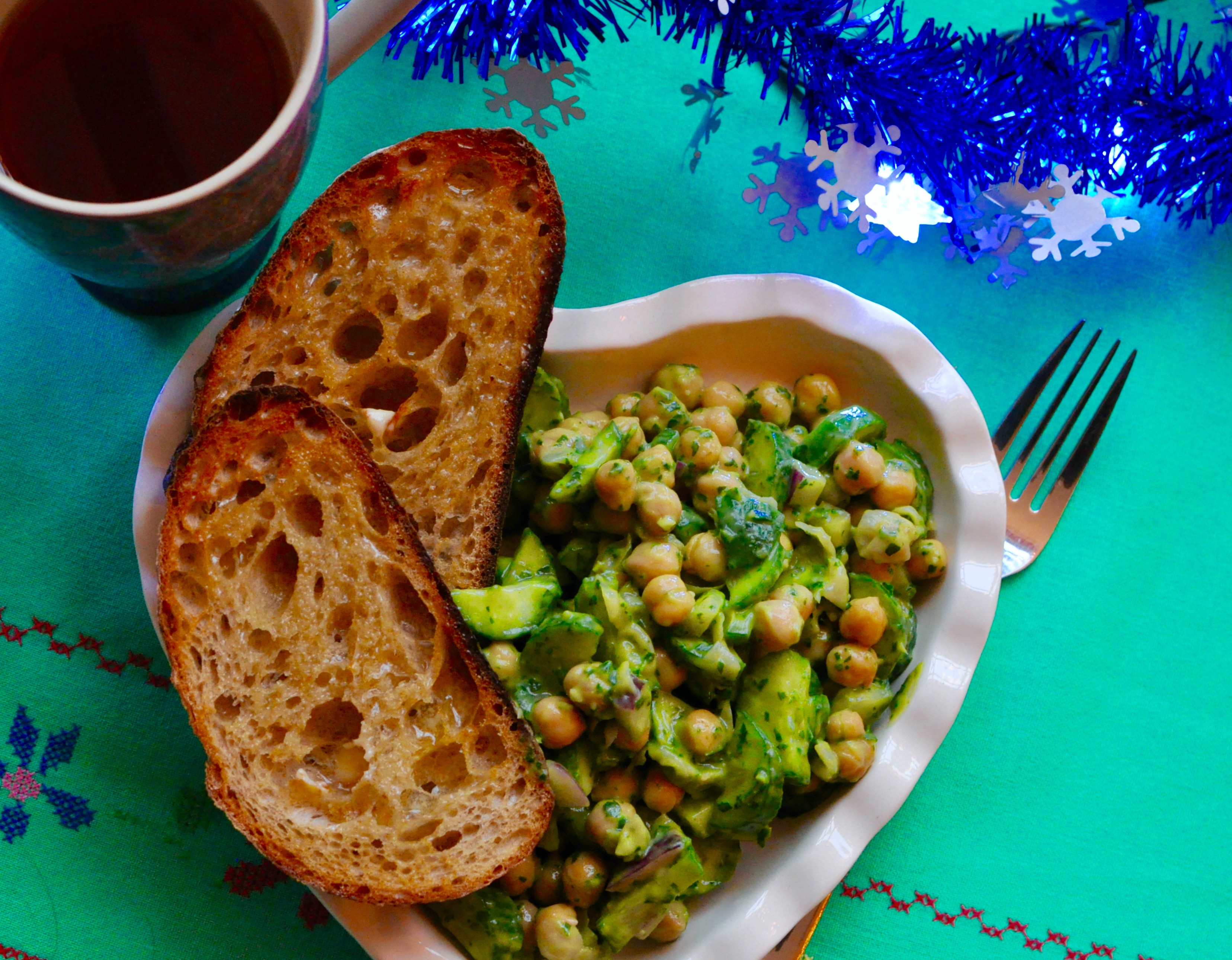 Heart-shaped plate full chickpea and cucumber salad and 2 pieces of sour dough toast.