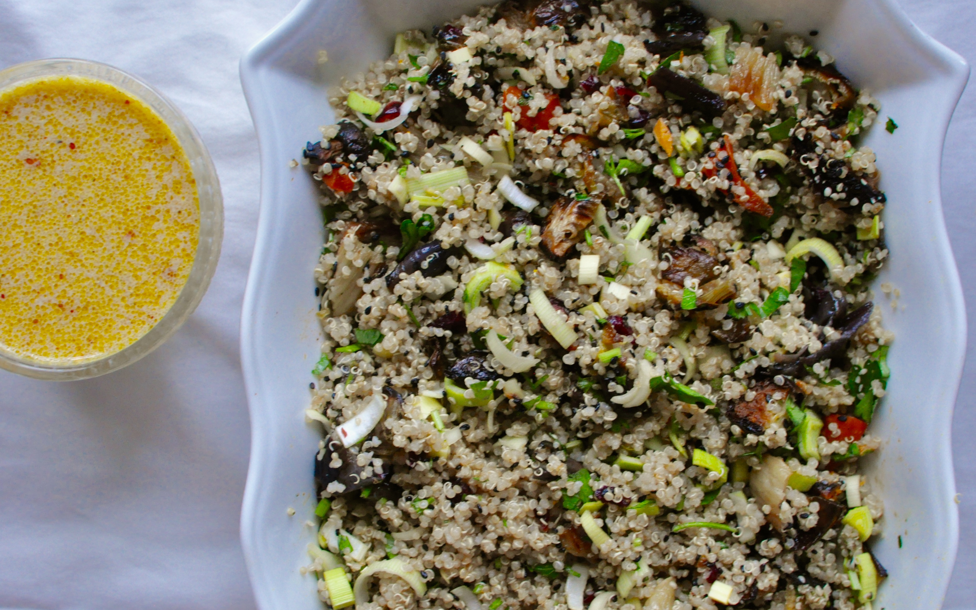White dish full of quinoa and roasted vegetable salad beside a glass container containing creamy orange salad dressing.