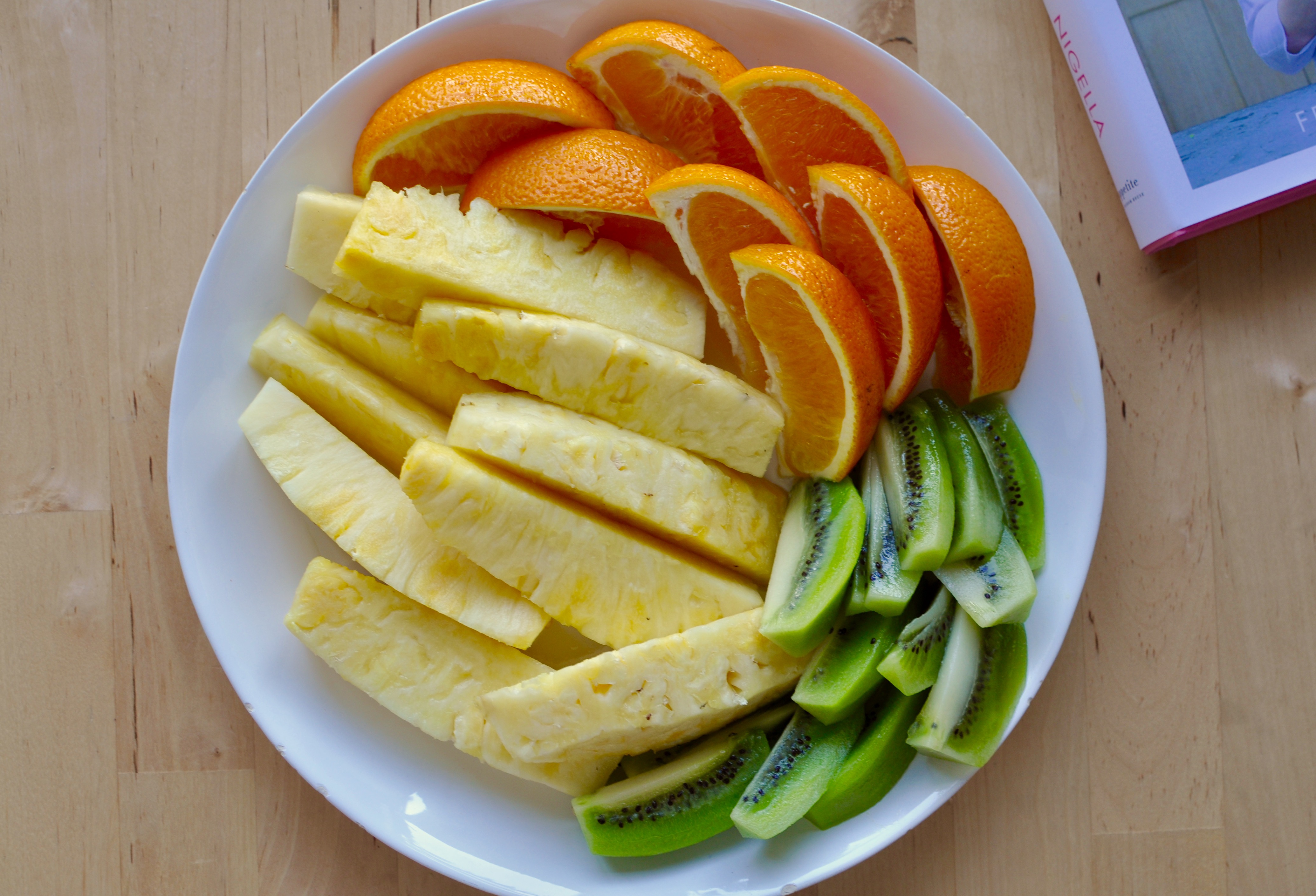 Shallow plate of fruit containing pineapple, oranges, and kiwi.