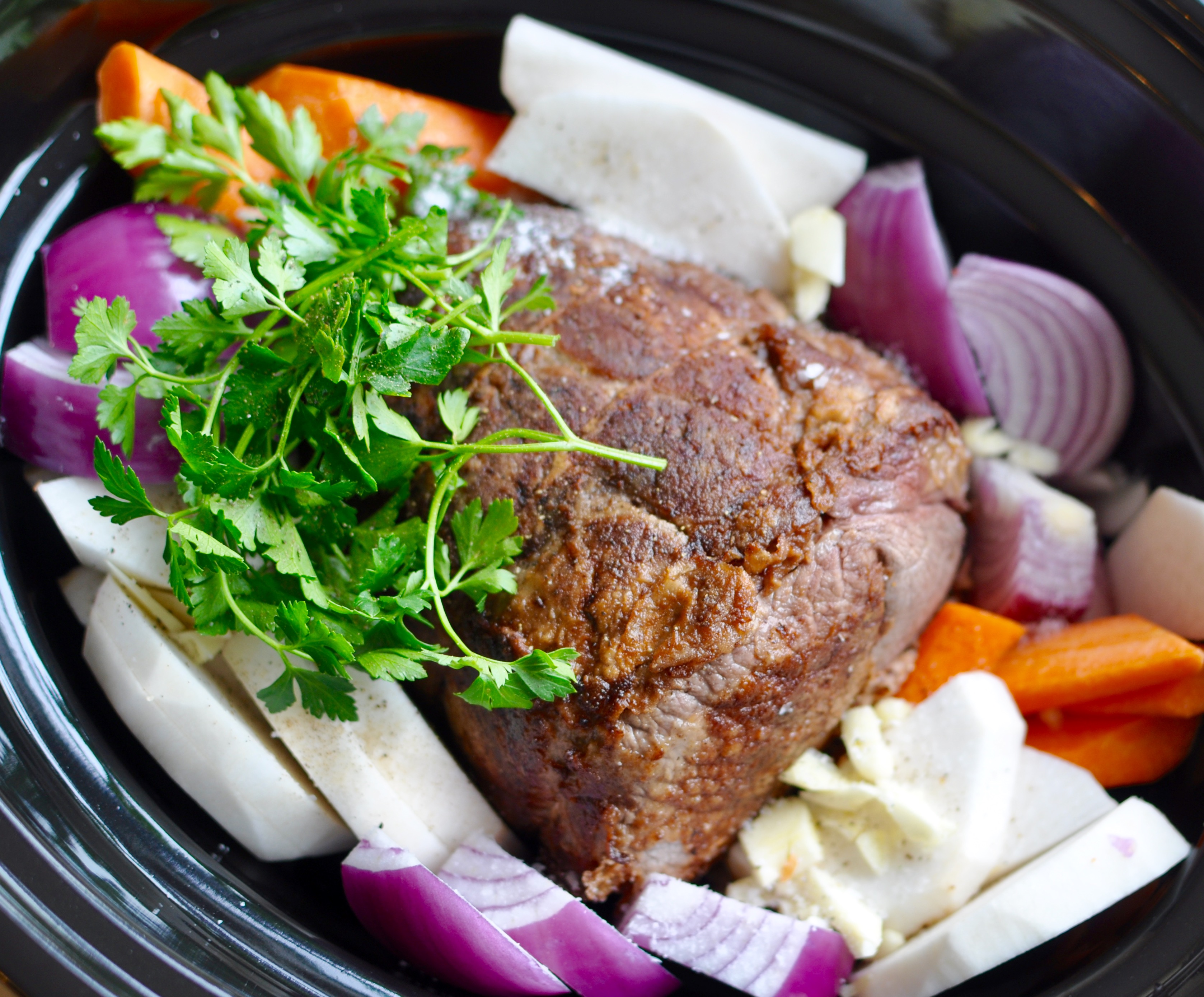 Pot roast and vegetables in a black slow cooker before cooking.