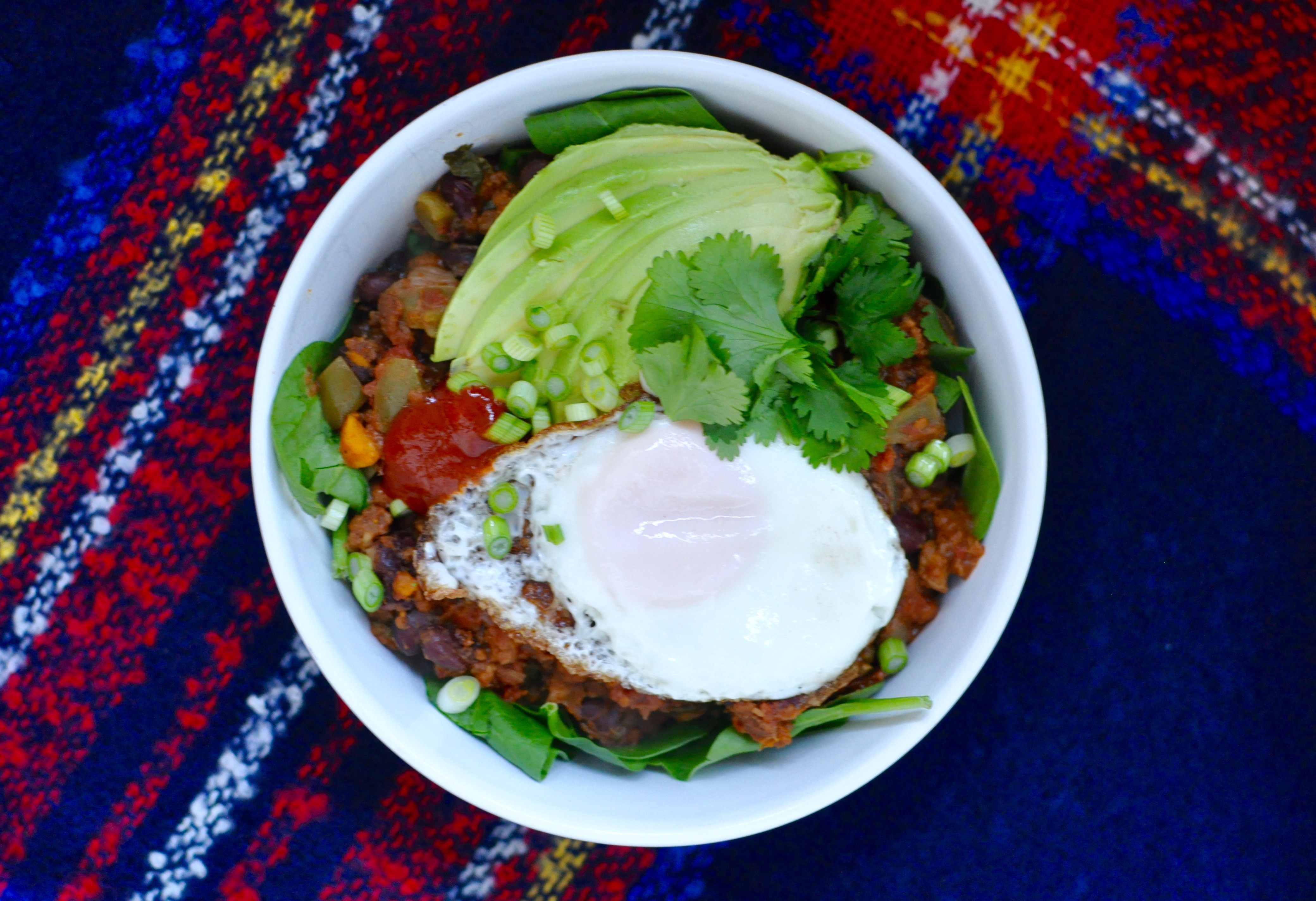 Vegetarian slow cooker chili in a shallow white bowl. The chili is topped with an egg, sliced avocado, and scallions.