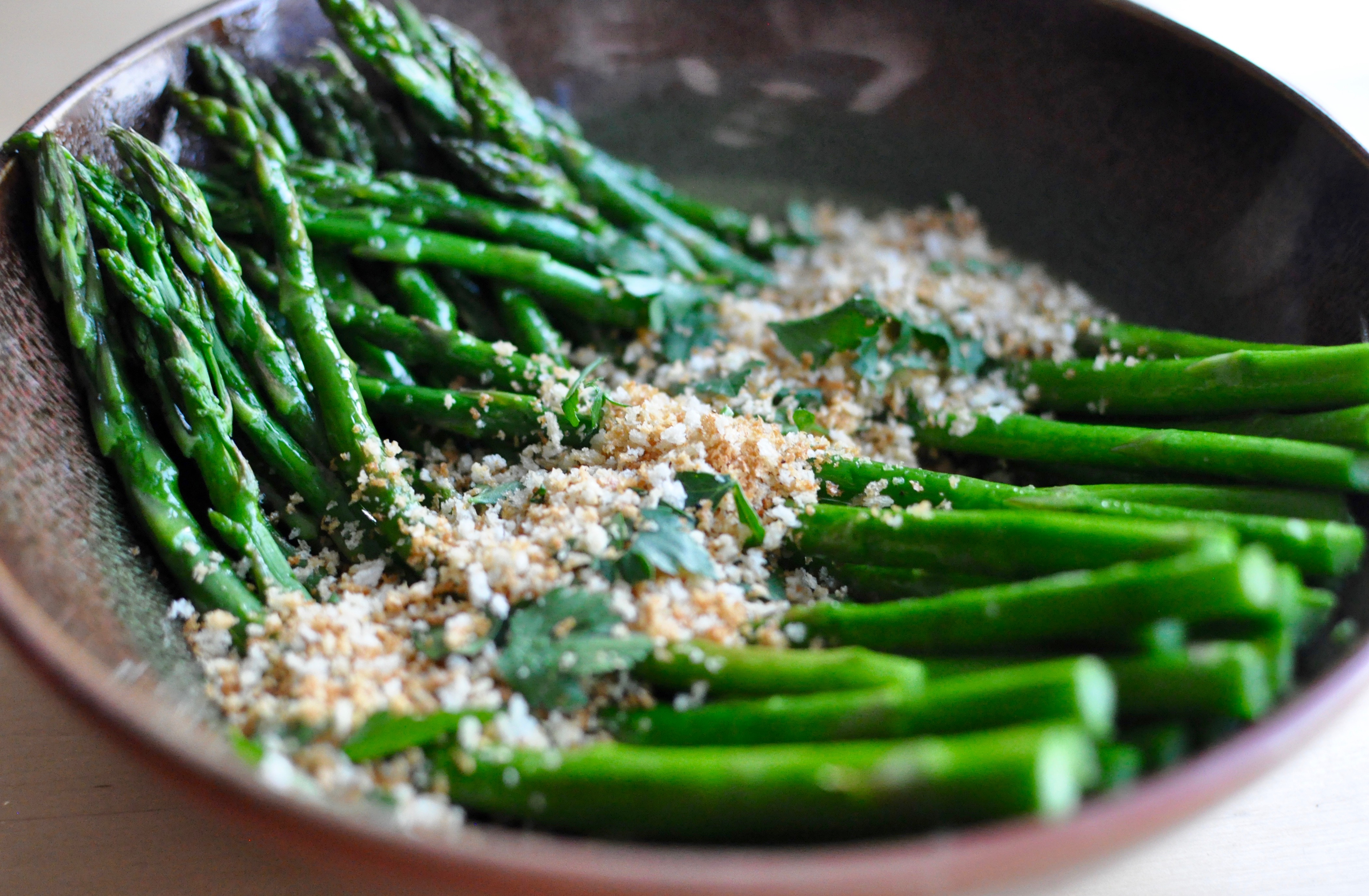 Earthenware shallow bowl with roasted asparagus, toasted breadcrumbs, and parsley.