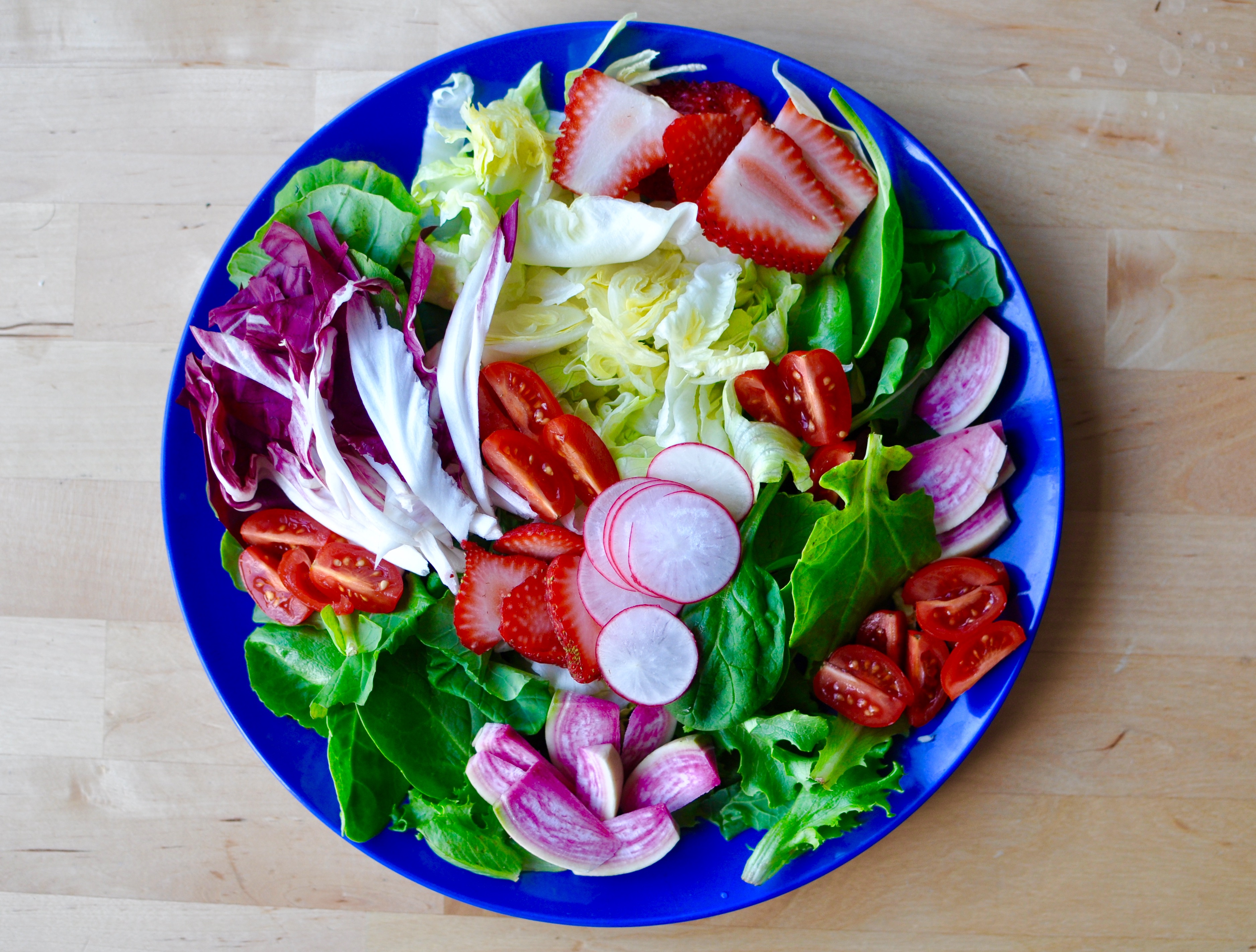 Large blue plate full of salad with iceberg lettuce, baby kale, radishes, tomatoes, and strawberries.