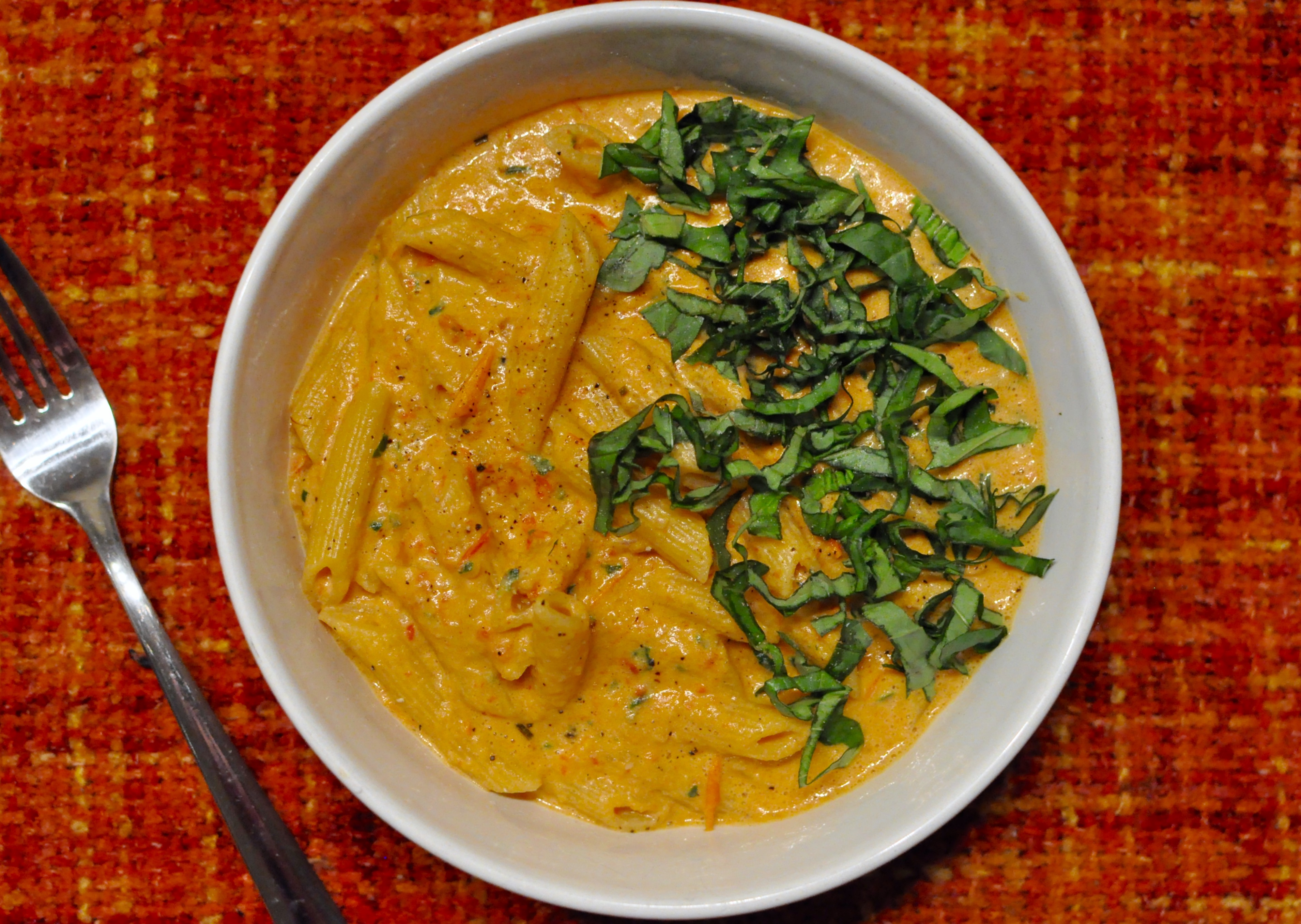 White bowl full of penne and a roasted red pepper blush sauce on an orange tablecloth.