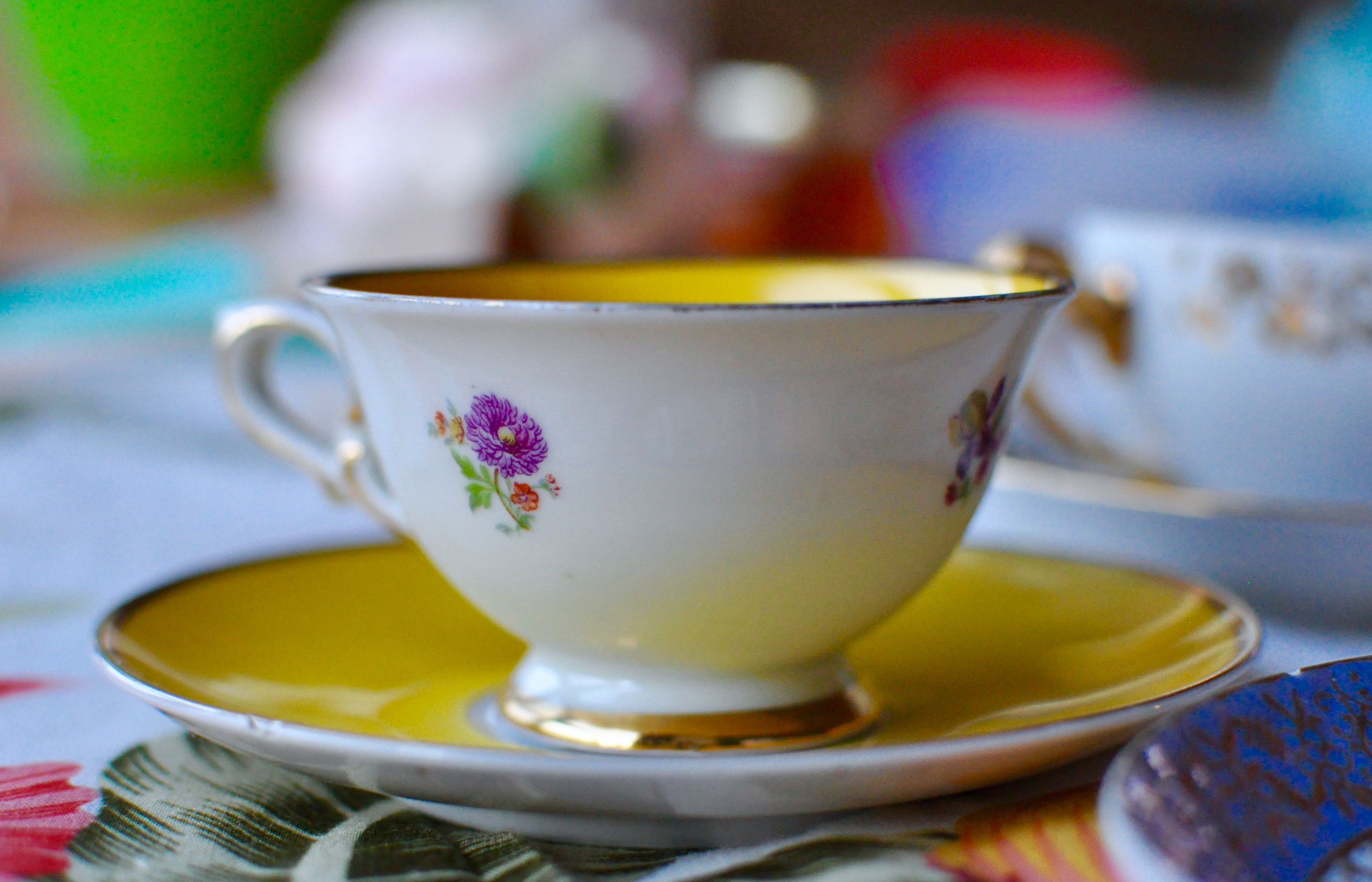 Colourful teacups on a flowered tablecloth, filled with pink watermelon gazpacho.