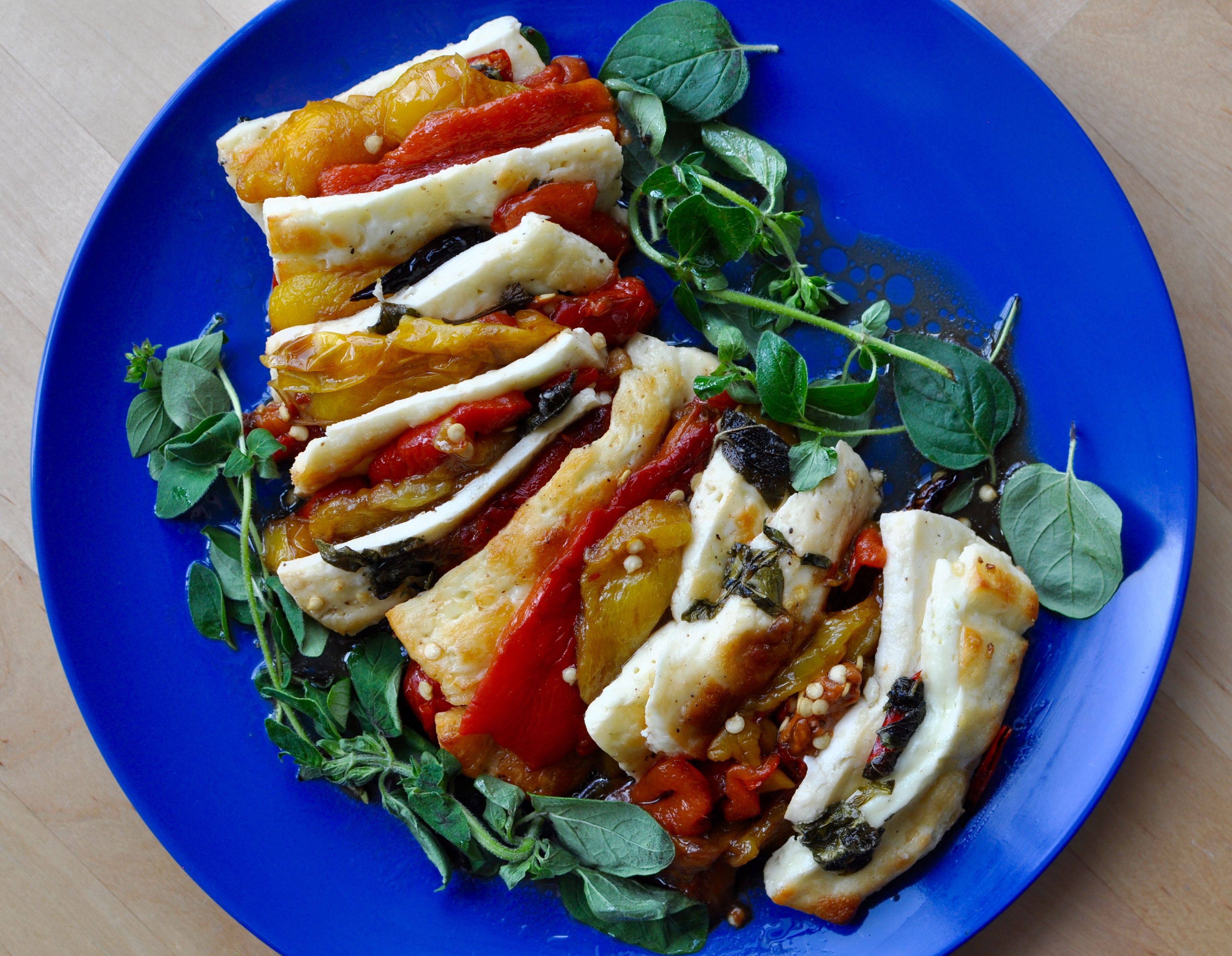 Slow roasted sweet peppers layered with slices of halloumi on a bright blue plate with decorative sprigs of halloumi cheese.