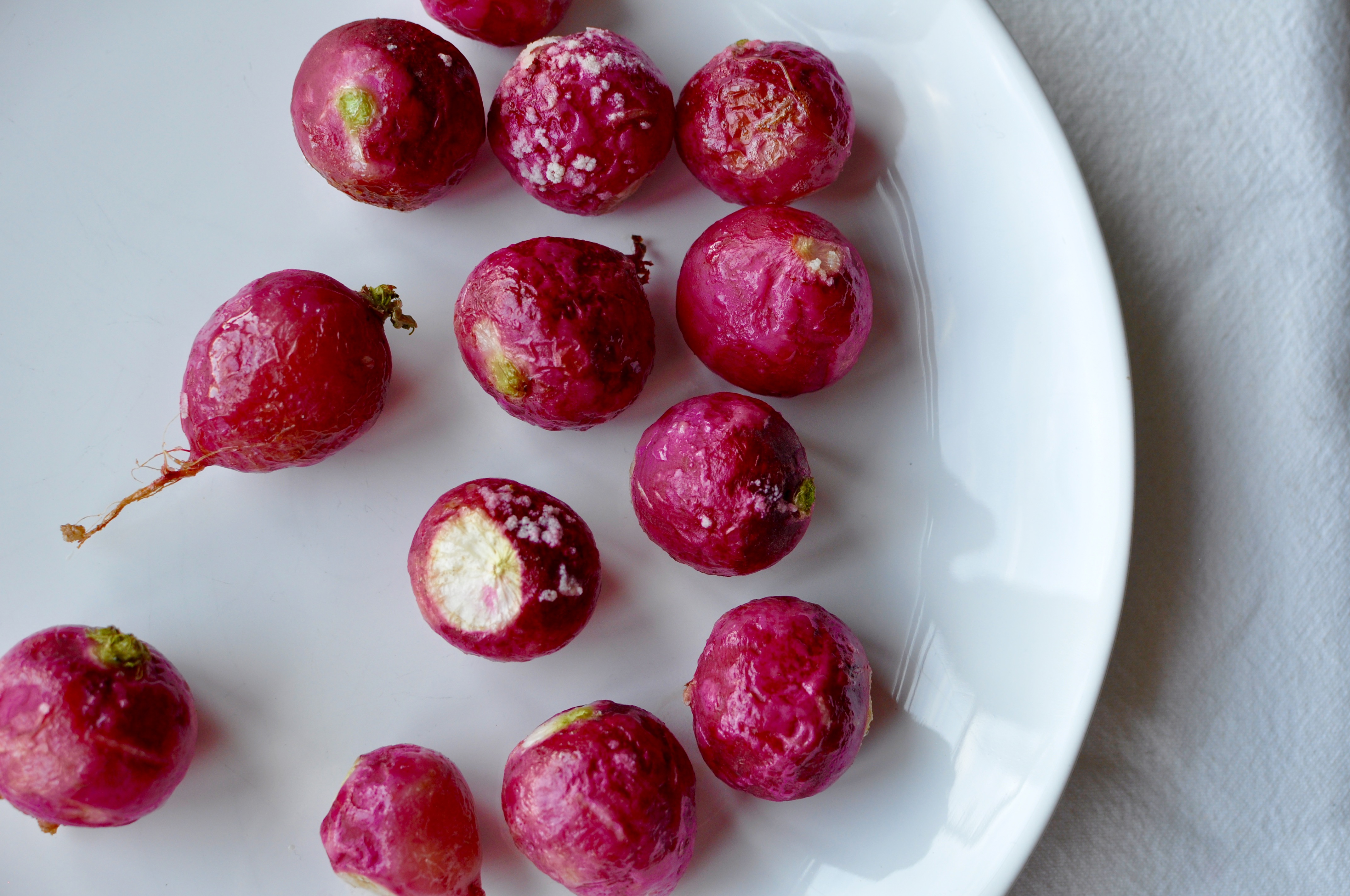 Roasted pink radishes on a white plate.