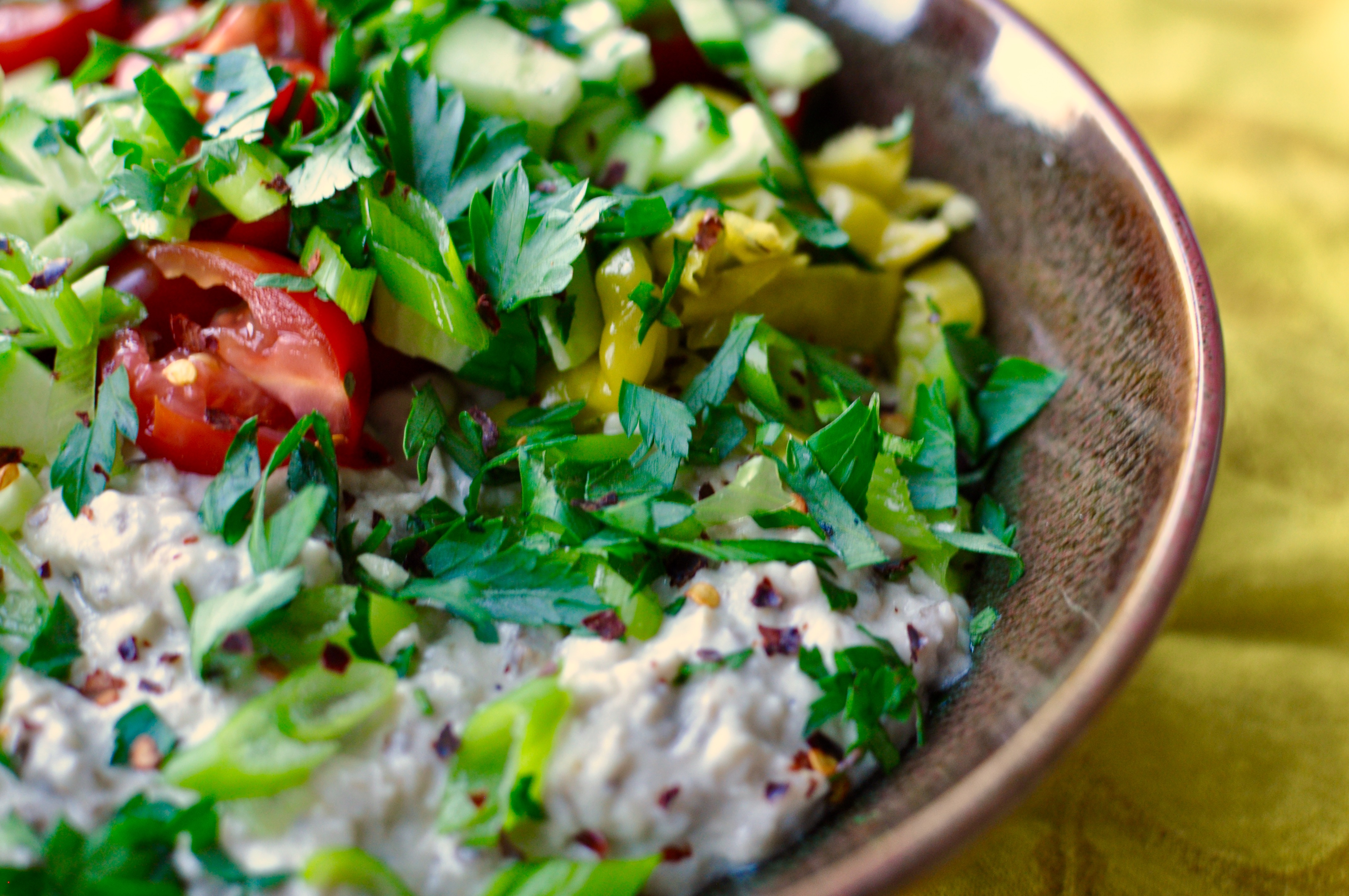 Brown shallow earthenware bowl filled with eggplant dip and with a topping of fattoush salad
