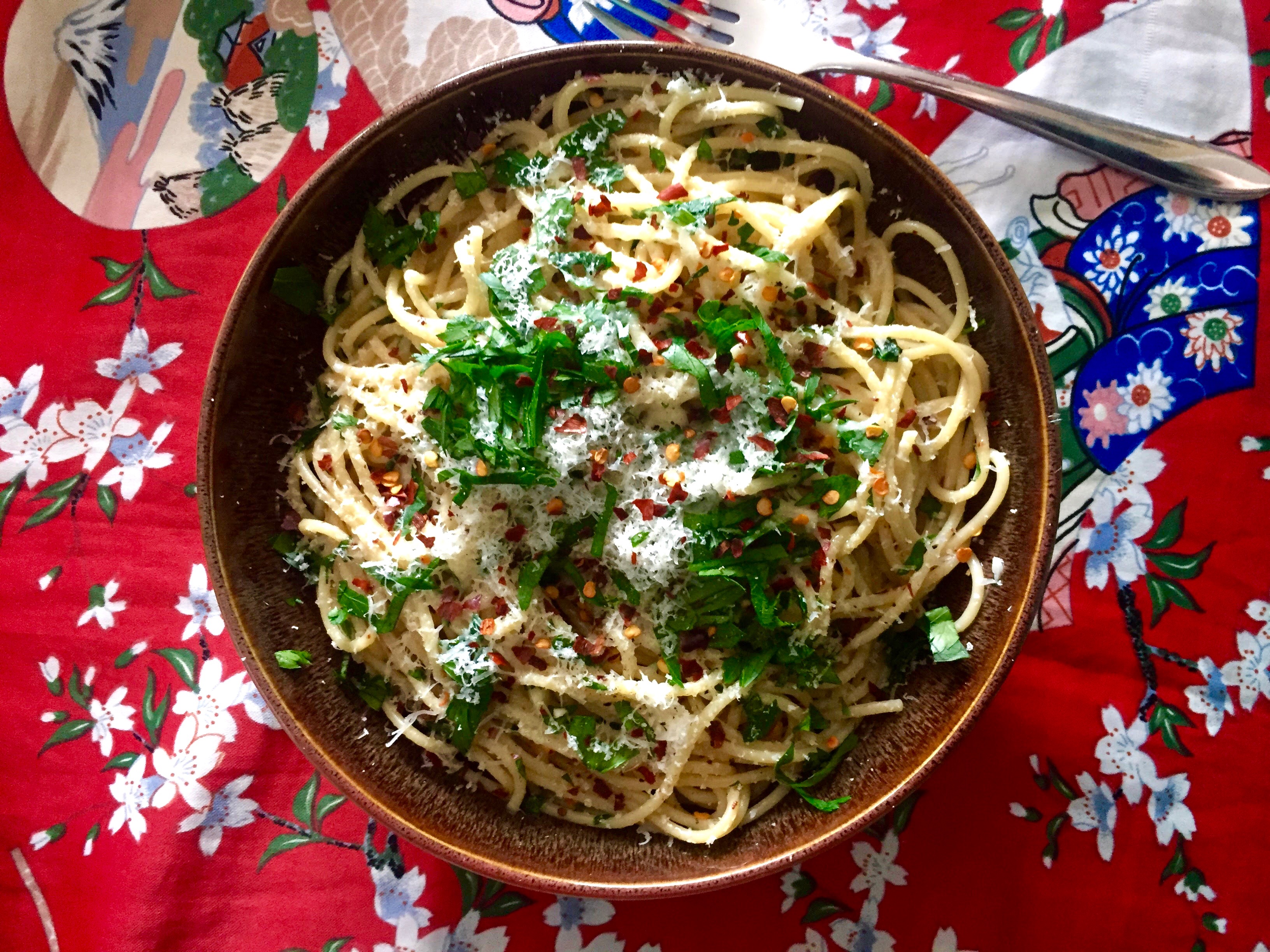 Spaghetti with Fresh Herbs, Chilies, Parmesan, and Black Pepper on a vivid red background.