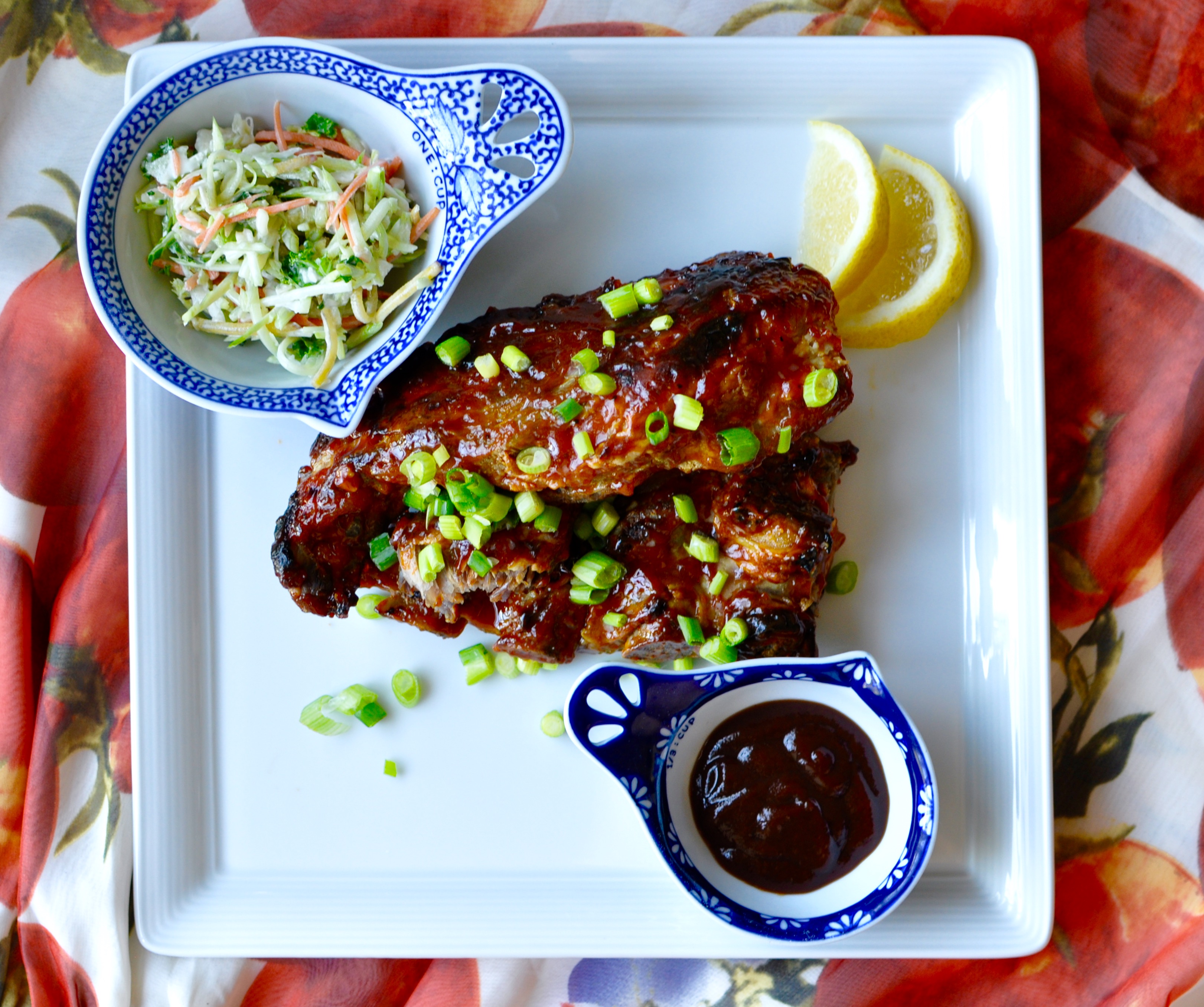 Ribs with scallions, coleslaw, and barbecue sauce in small dishes on a rectangular plate.