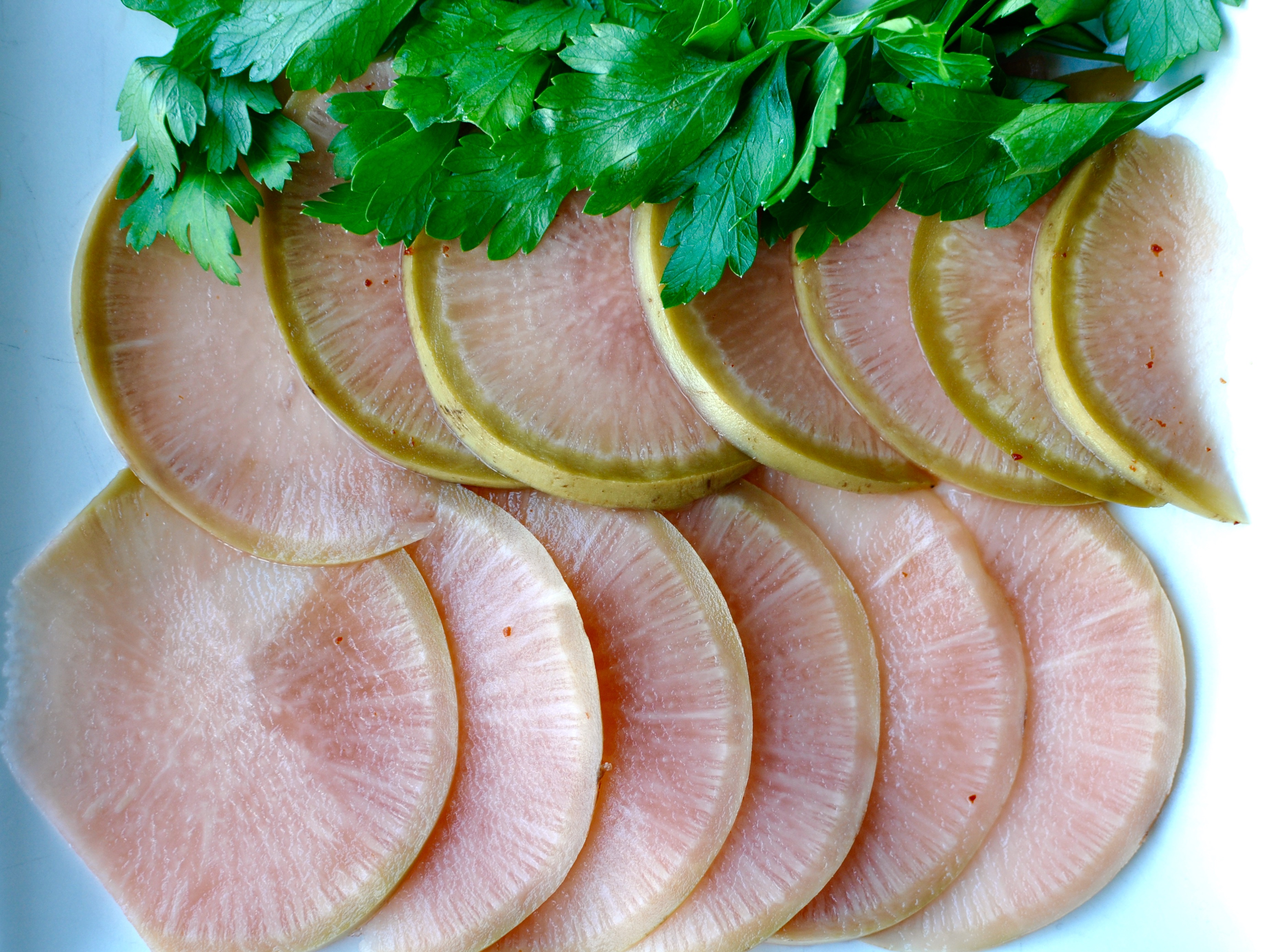 Thinly sliced watermelon radish on a white background with parsley.