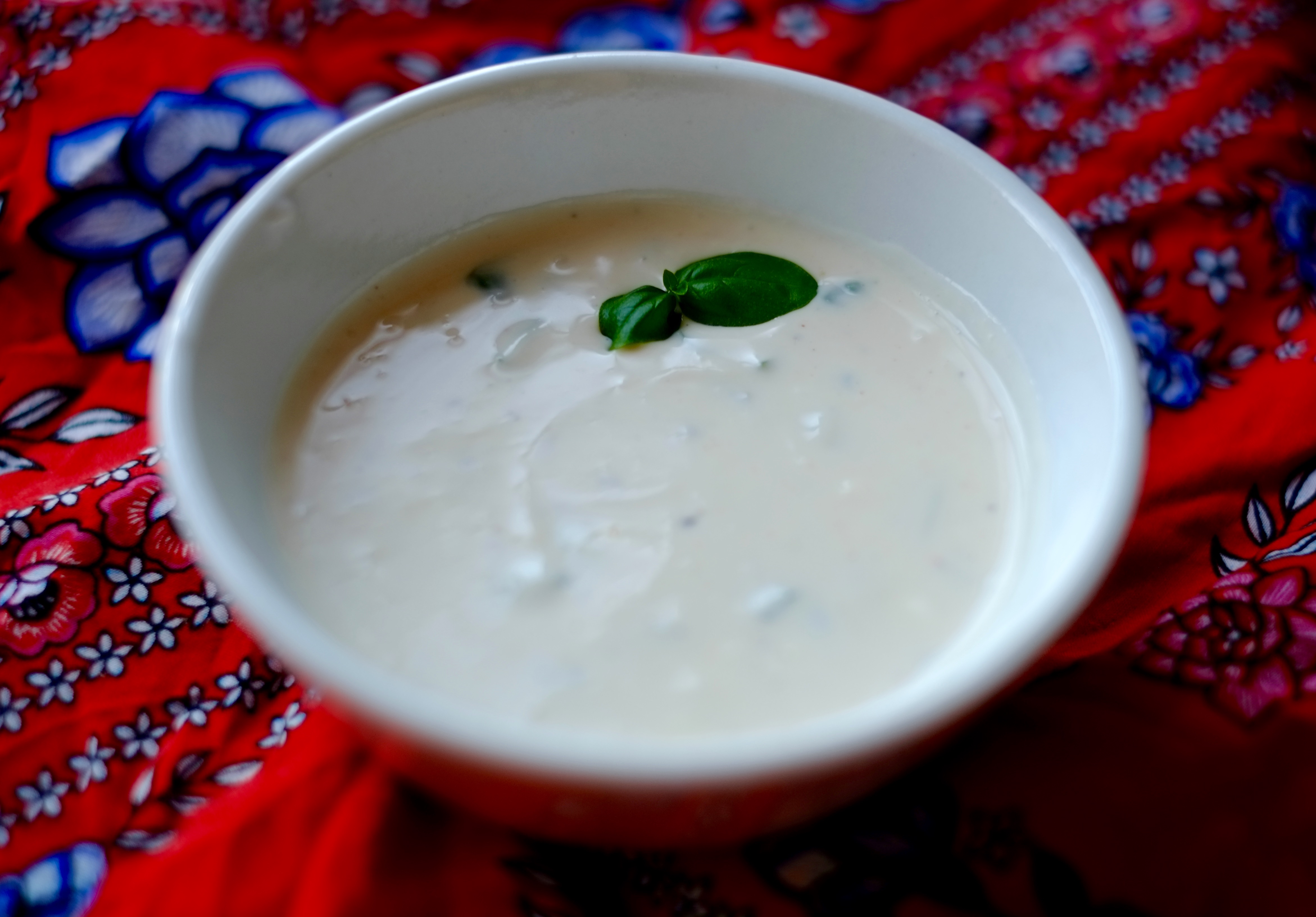 A small white bowl full of salad dressing and garnished with a small basil leaf on an orange and blue background.