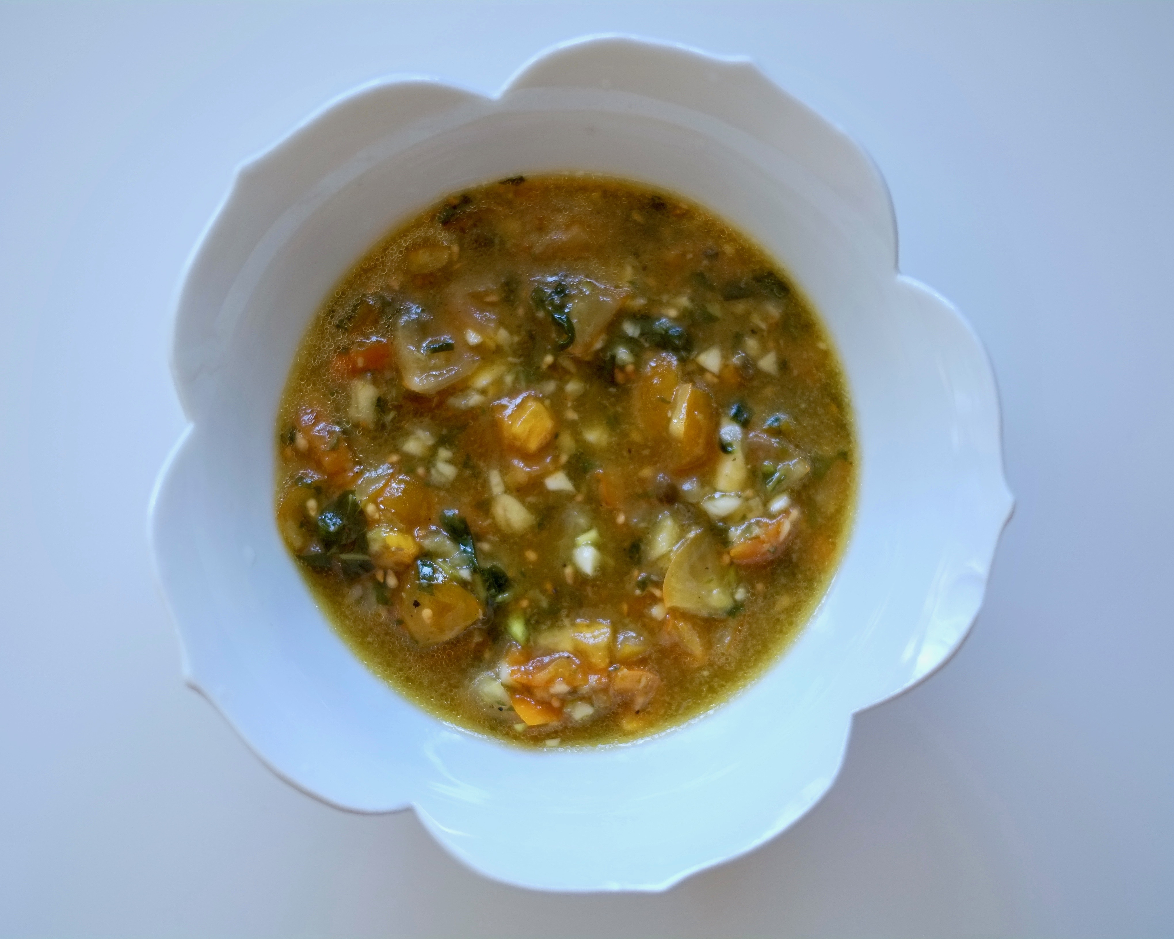 Lotus-shaped white bowl on a white background filled with a tomato and basil salad dressing.
