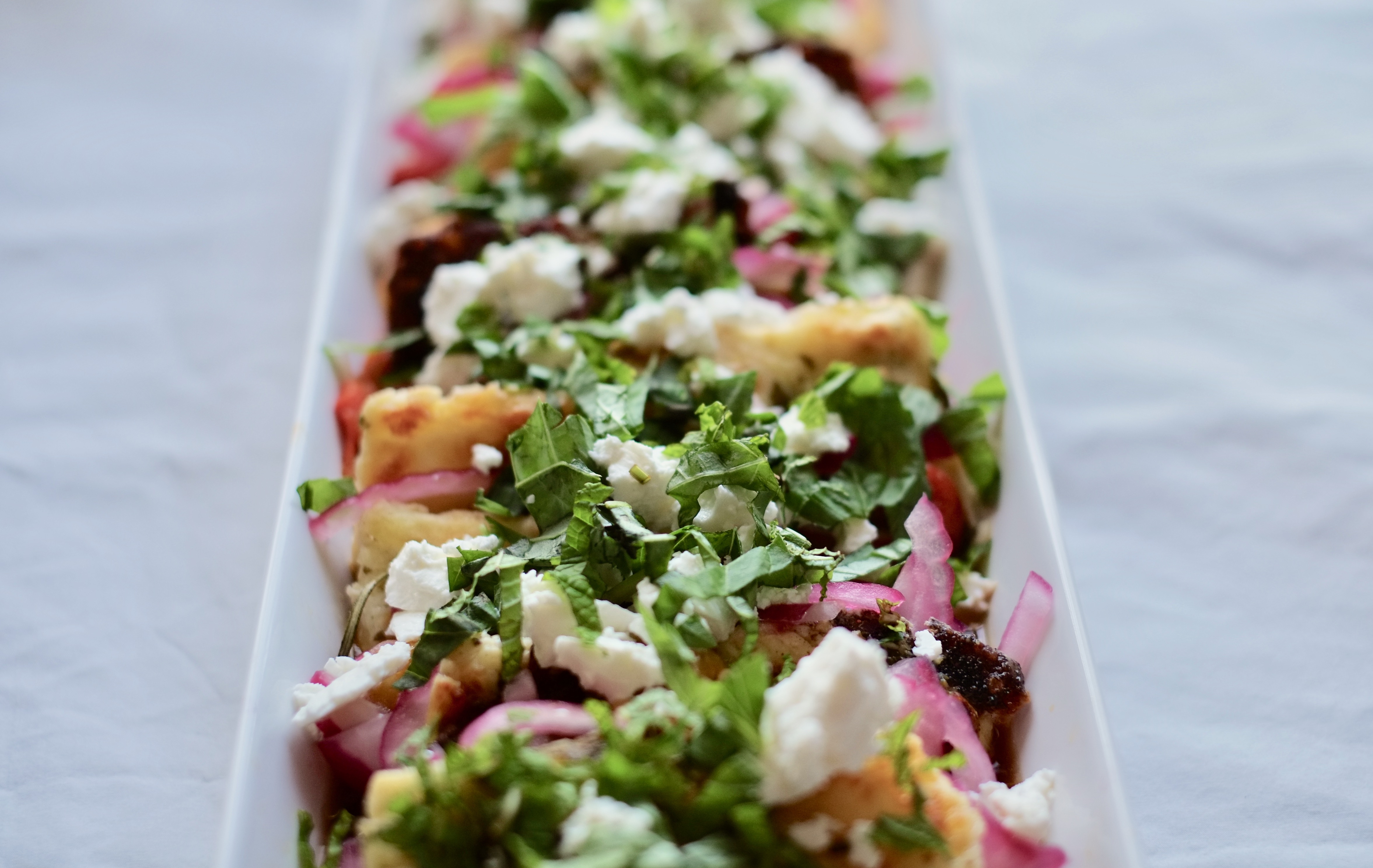 Halloumi Salad with Roasted Red and JalapeÃ±o Peppers, Pickled Red Onions, and Mint in a narrow white serving dish on a white tablecloth.