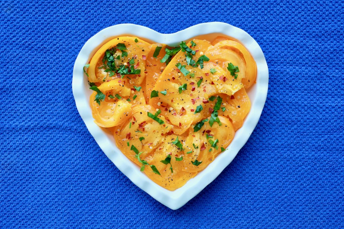 Yellow tomato salad on a white heart-shaped plate on a blue background.