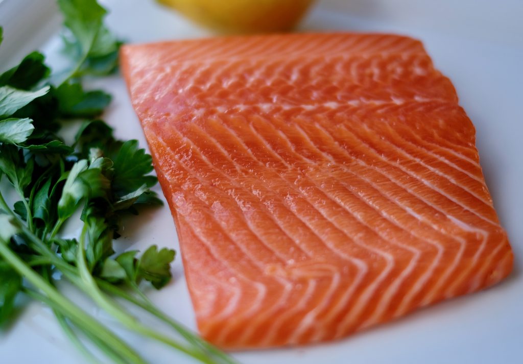 Close-up of a raw trout fillet beside a bunch of fresh parsley on a white background.